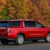 Rear side view of red 2022 Chevrolet Suburban Premier parked against backdrop of colorful fall leaves