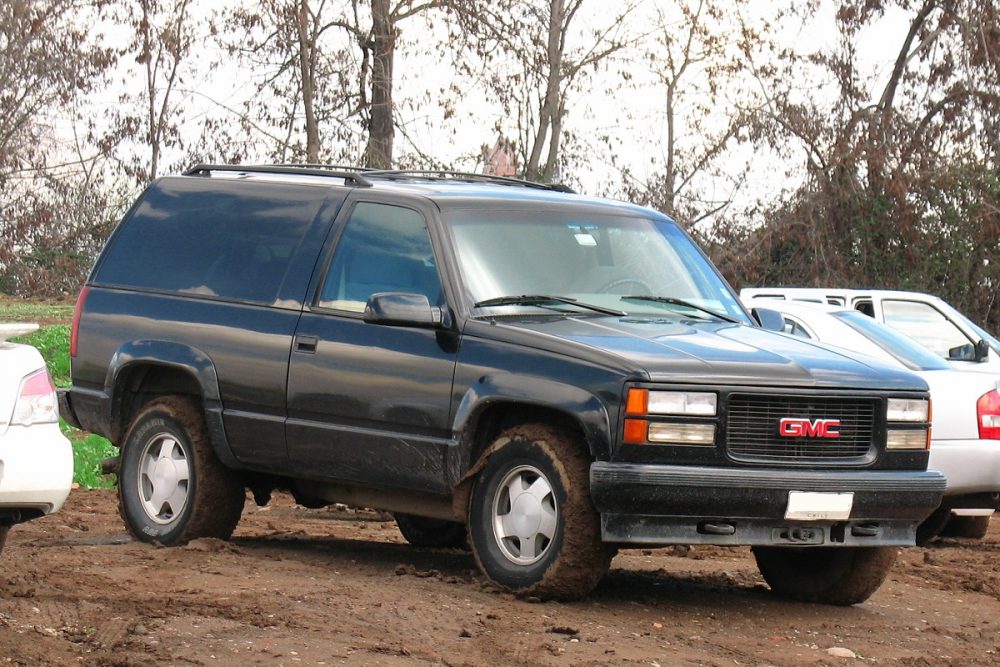 A black 1996 GMC Yukon is parked on dirt next to other vehicles