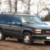 A black 1996 GMC Yukon is parked on dirt next to other vehicles