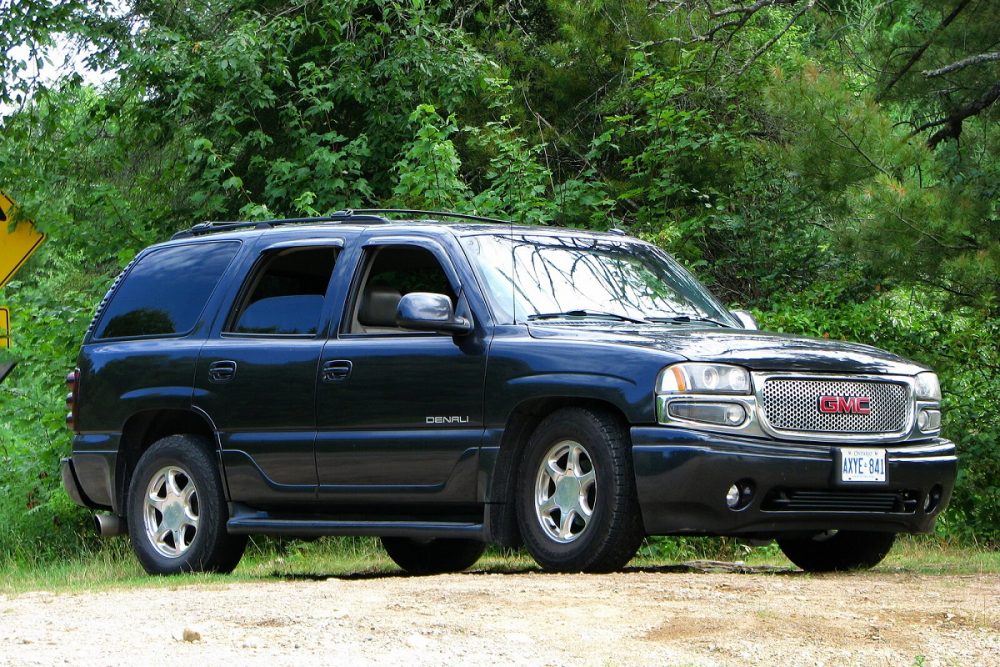 A dark blue 2002 GMC Yukon Denali is parked on grass in front of trees