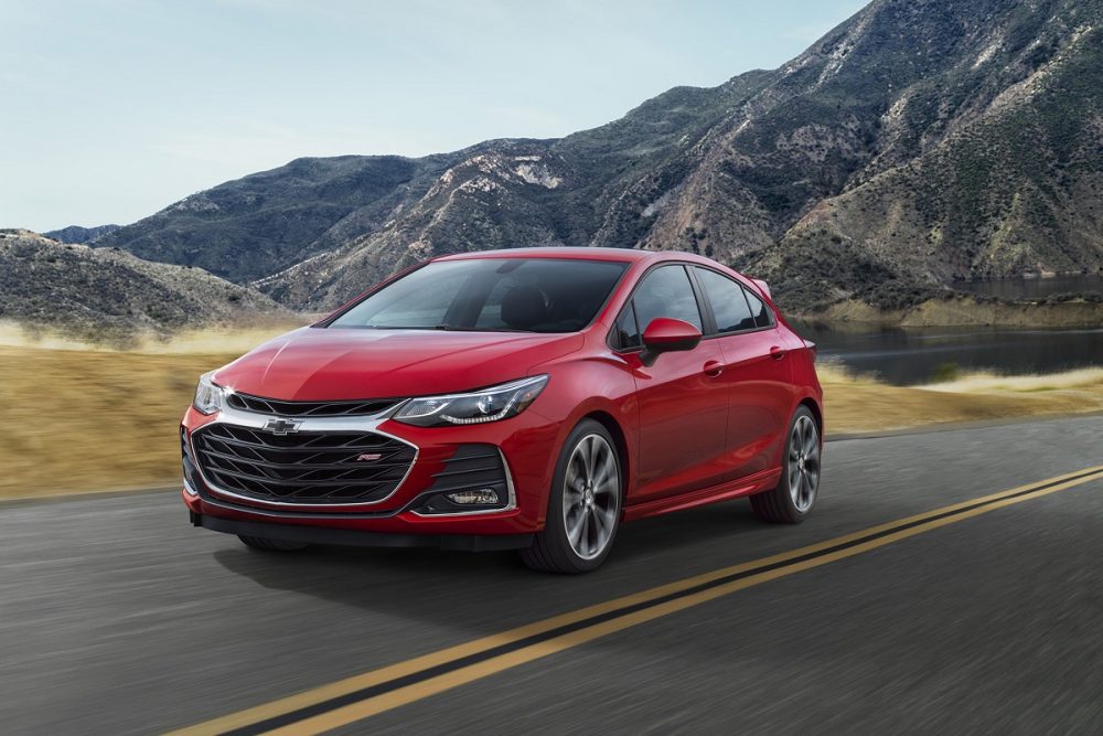 A red 2019 Chevrolet Cruze Hatchback drives on a highway road among the mountains