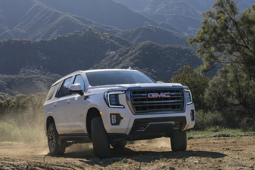 A white 2022 GMC Yukon AT4 drives on a gravel road among the mountains