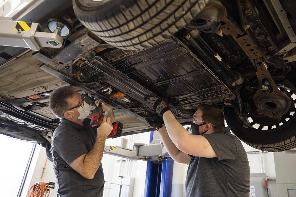 Two mechanics remove a lithium-ion battery from a car