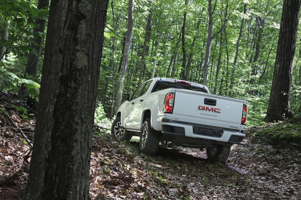 Rear side view of 2022 GMC Canyon AT4 driving in hilly woods