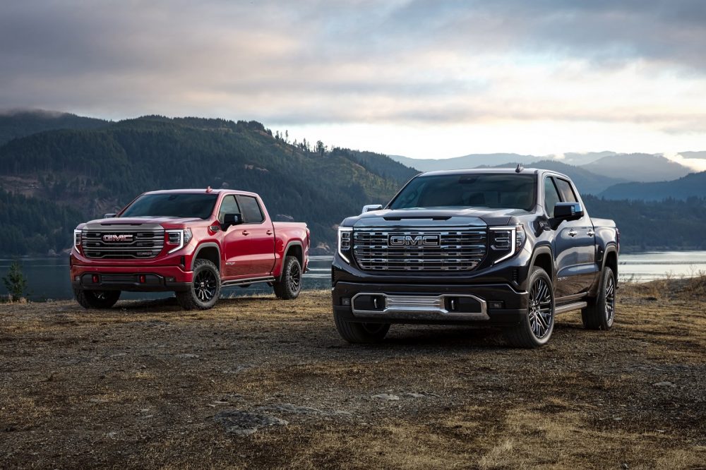 Front side views of red 2022 GMC Sierra AT4X and black GMC Sierra Denali Ultimate parked side by side with mountains and lake in background