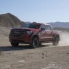 Front side view of red 2022 GMC Sierra AT4X driving off-road and kicking up dust