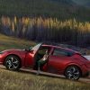 A red Kia EV6 is parked on a hill in a scenic area with someone sitting in the front seat with the door open