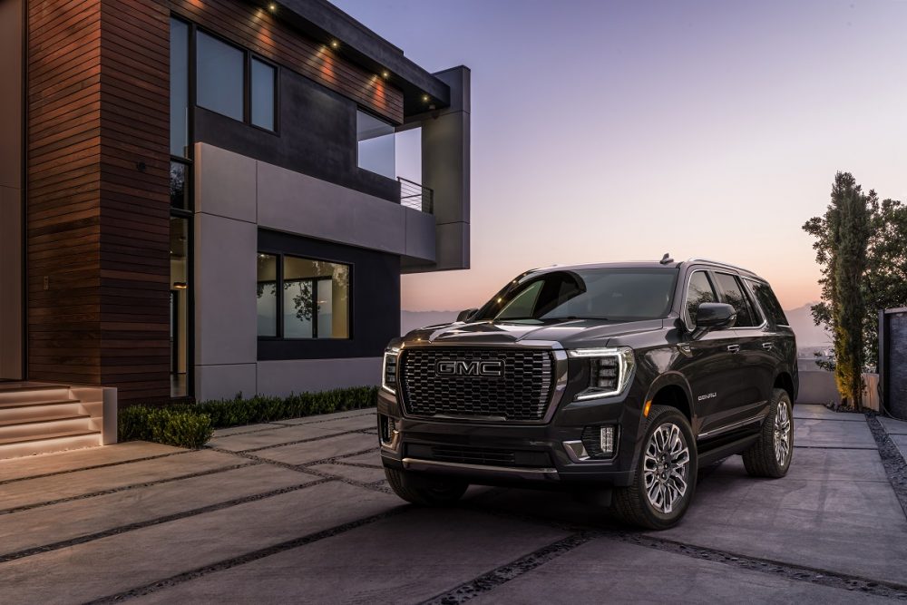 A black 2023 GMC Yukon Denali Ultimate is parked in front of a modern home at sunset