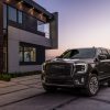 A black 2023 GMC Yukon Denali Ultimate is parked in front of a modern home at sunset