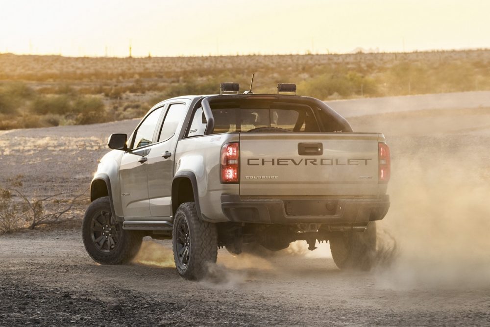 Rear side view of tan 2022 Chevrolet Colorado ZR2 kicking up dust cloud at sunset