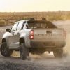 Rear side view of tan 2022 Chevrolet Colorado ZR2 kicking up dust cloud at sunset