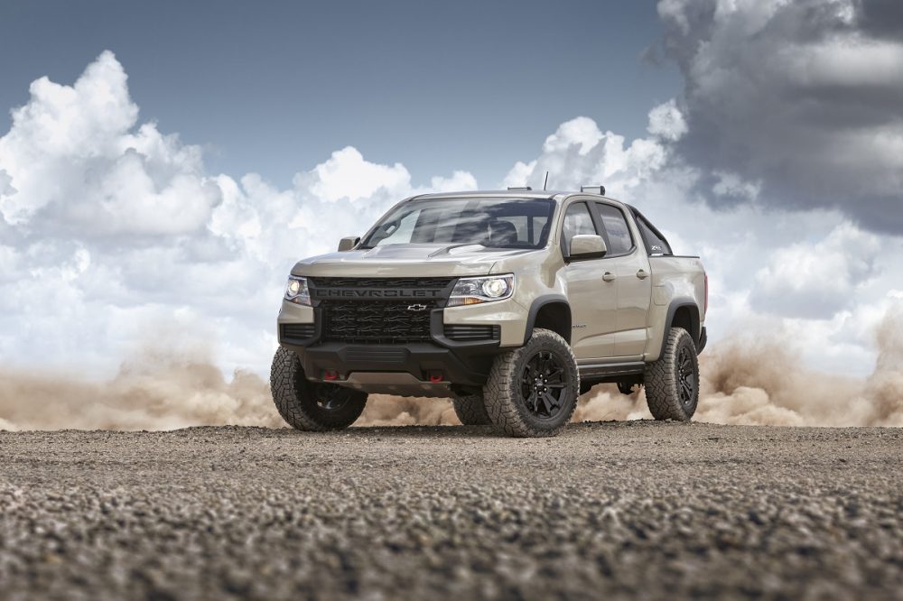 Front side view of tan 2022 Chevrolet Colorado ZR2 with clouds and dust clouds in background