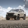 Front side view of tan 2022 Chevrolet Colorado ZR2 with clouds and dust clouds in background