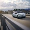 Front side view of 2023 Chevrolet Bolt EV driving down across bridge with city skyline in background