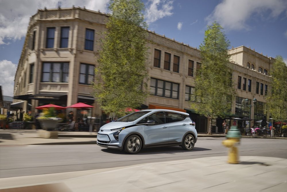 Side view of 2023 Chevrolet Bolt EV driving down city street with large building in background