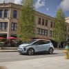 Side view of 2023 Chevrolet Bolt EV driving down city street with large building in background