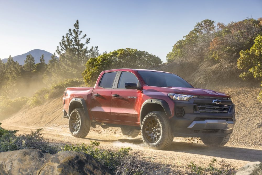 Front side view of red 2023 Chevrolet Colorado Trail Boss driving down dirt road