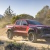 Front side view of red 2023 Chevrolet Colorado Trail Boss driving down dirt road