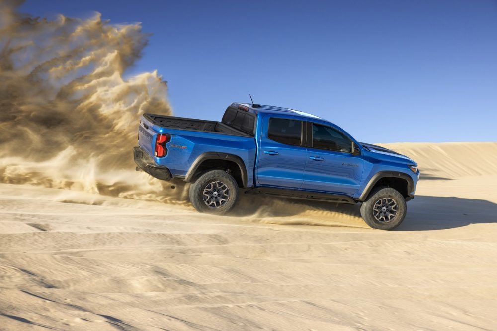 Side view of blue 2023 Chevrolet Colorado ZR2 kicking up dust cloud in desert