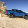 Side view of blue 2023 Chevrolet Colorado ZR2 kicking up dust cloud in desert