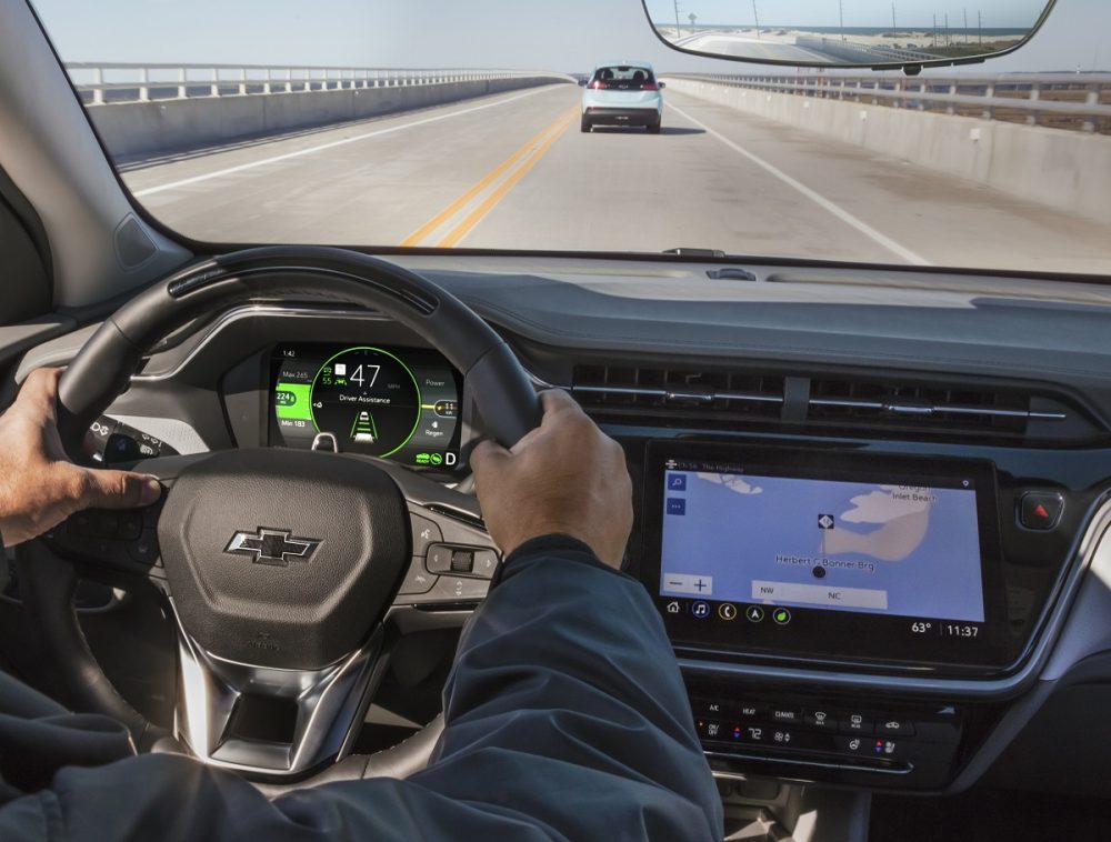 Foreground: Hands on Chevrolet Bolt EUV steering wheel. Background: View of road through windshield.