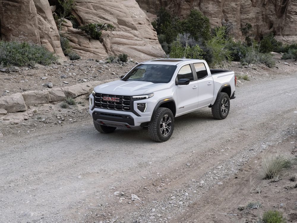 Front overhead side view of white 2023 GMC Canyon AT4 driving down gravel road