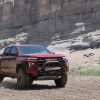 Front side view of red 2023 GMC Canyon AT4X kicking up dust cloud on rocky trail