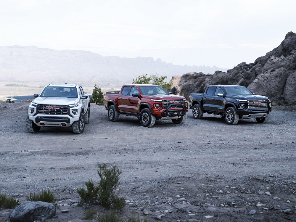 From left, the 2023 GMC Canyon AT4, Canyon AT4X, and Canyon Denali sit parked next to each other against a mountain backdrop