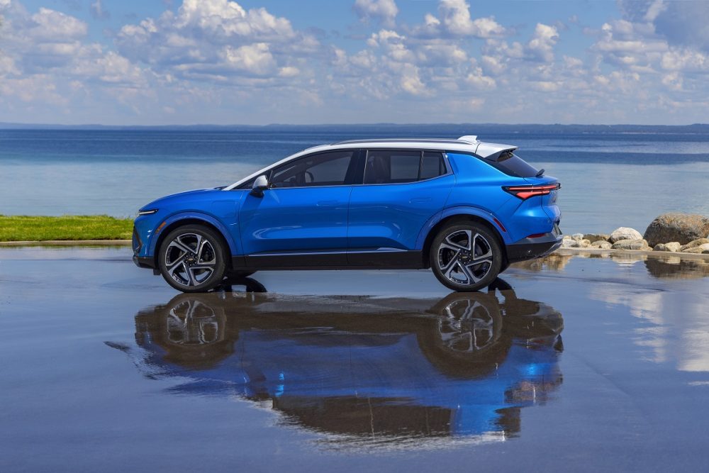 Side view of 2024 Chevrolet Equinox EV 3LT parked in front of water and reflected on wet road