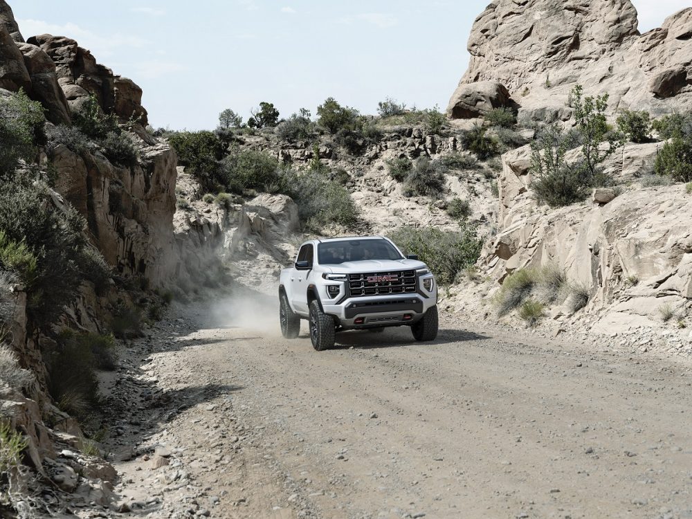 Front view of white 2023 GMC Canyon AT4 driving on dirt road in rocky canyon