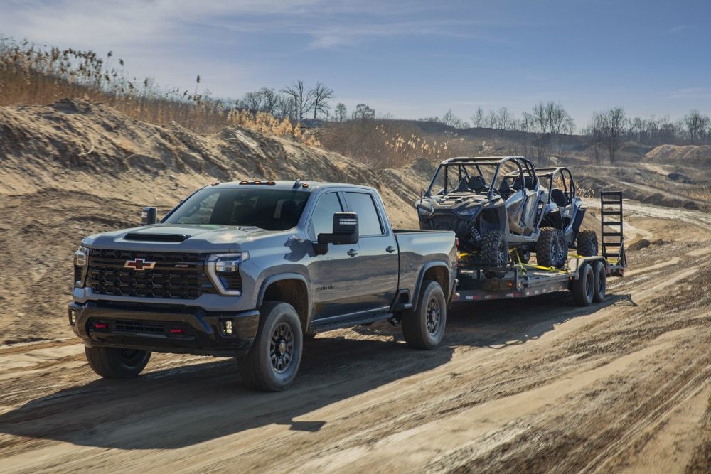 Front side view of 2024 Chevrolet Silverado HD ZR2 towing side-by-sides on a dirt trail
