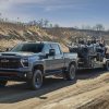 Front side view of 2024 Chevrolet Silverado HD ZR2 towing side-by-sides on a dirt trail