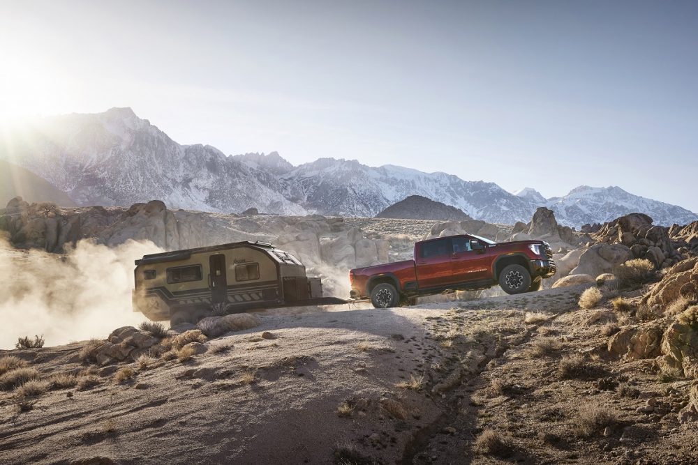 Side view of 2024 GMC Sierra HD AT4X towing a trailer across rocky mountain terrain