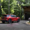 rear side view of red 2024 Chevrolet Traverse RS parked in front of a house in the woods