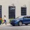 Front side view of blue 2024 Buick Enclave parked in front of building as two people approach from the left