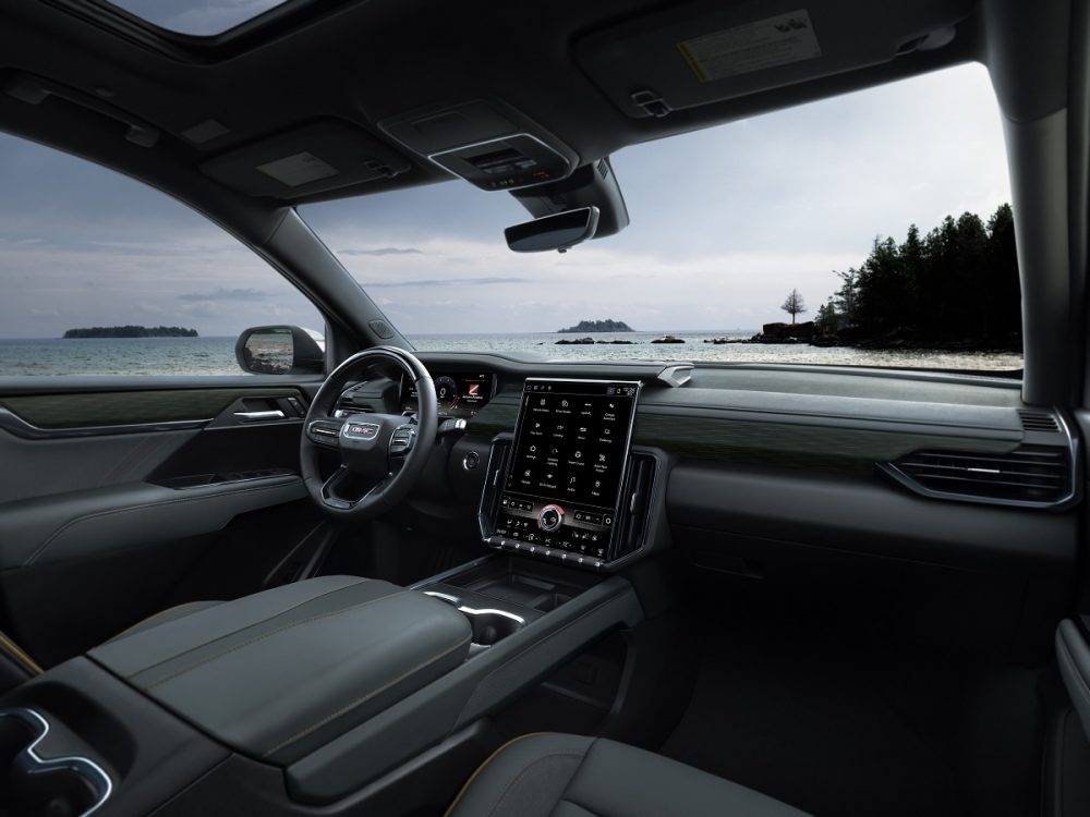 Side view of 2024 GMC Acadia AT4 front seats, steering wheel, and dashboard with 15-inch portrait touch screen