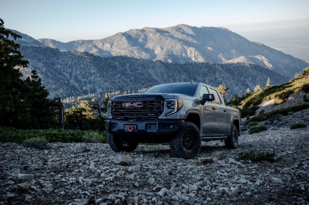 Front side view of gray 2024 GMC Sierra 1500 AT4X AEV Edition parked on rocky ground with mountains in background