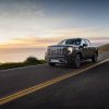 Front side view of 2024 GMC Sierra Denali Ultimate driving near water at sunset