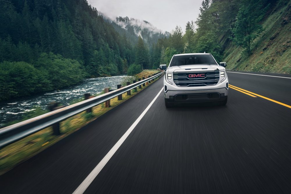 Front view of 2024 GMC Sierra 1500 SLT driving down road next to river in mountainous forest