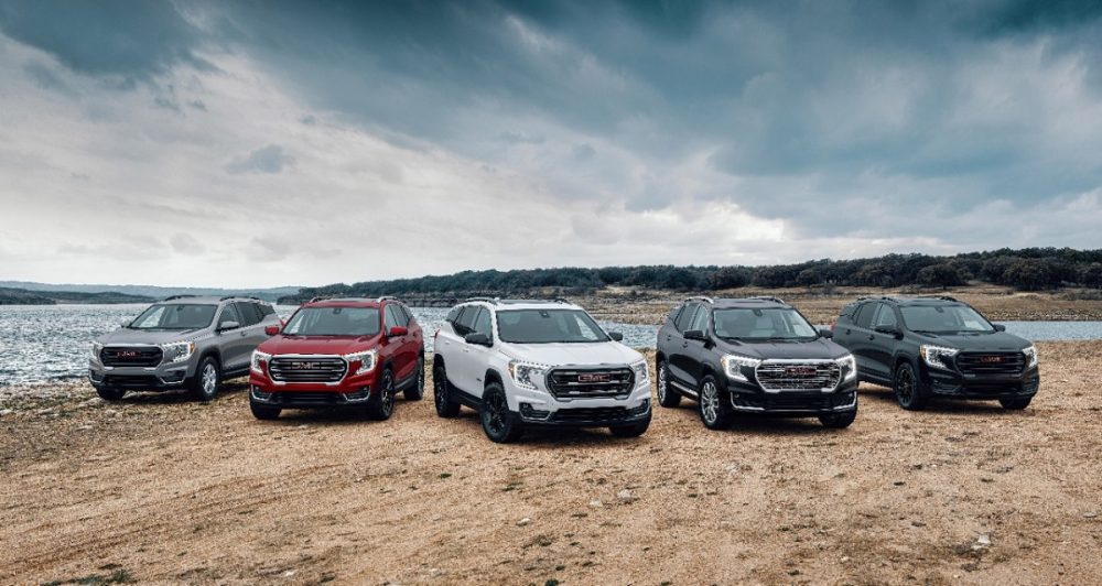 The 2024 GMC Terrain trim lineup is shown against a backdrop of sky and water. From left to right: SLE, SLT, AT4, Denali, Elevation Edition