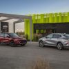 Two 2024 Buick Envista models are parked nose to nose in front of a building. A Buick Envista Sport Touring in Cinnabar Metallic is on the left, and a Buick Envista Avenir in Moonstone Gray Metallic is on the right.