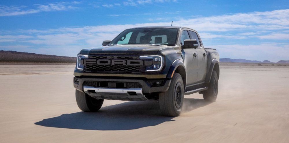 A 2024 Ford Ranger Raptor drivers through a stark desert against a clear blue sky