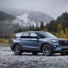 A 2025 Ford Explorer ST in Vapor Blue Metallic sits on a rocky beach in the wilderness. A foggy mountain looms in the background.