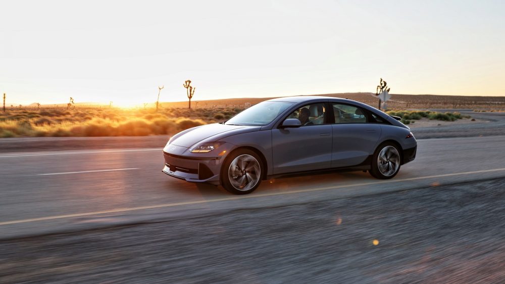 Side view of a gray 2024 Hyundai Ioniq 6 driving down a desert road as the sun sets