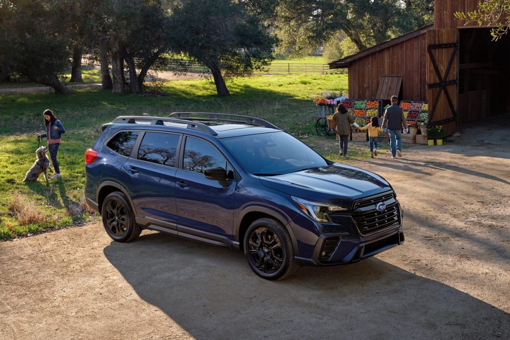 Aerial 3/4 view of a Subaru Ascent parked in front of a barn with people walking around the vehicle and nearby.