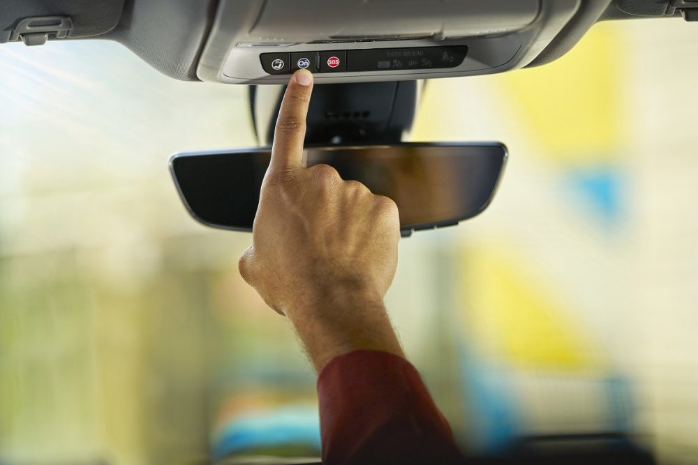 A person pushes the blue OnStar button inside a General Motors vehicle