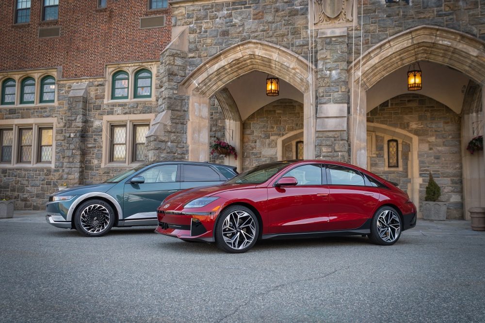 A green 2024 Hyundai Ioniq 5 and a red 2024 Hyundai Ioniq 6 are parked next to each other in front of an old stone building