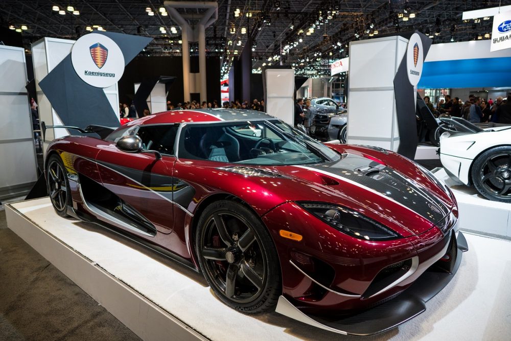 Three-quarter angle of a deep red Koenigsegg Regera on a platform at the New York Auto Show floor in 2018