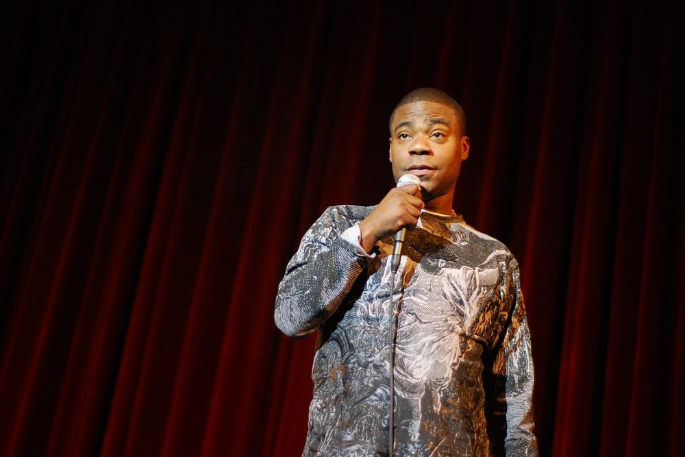 Comedian Tracy Morgan standing on a stage holding a microphone, in front of a red curtain