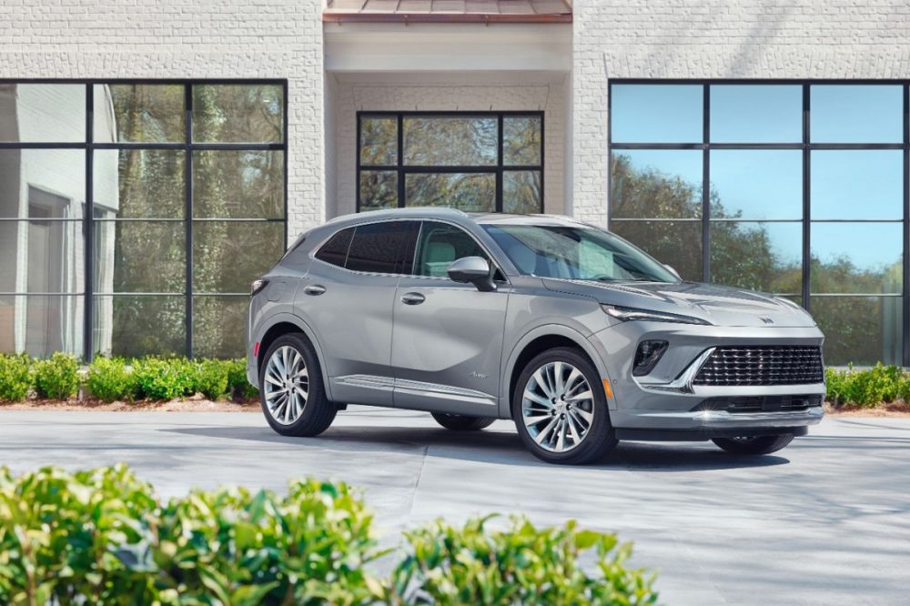 Front 3/4 view of a Moonstone Gray Metallic 2024 Buick Envision Avenir parked in front of a building